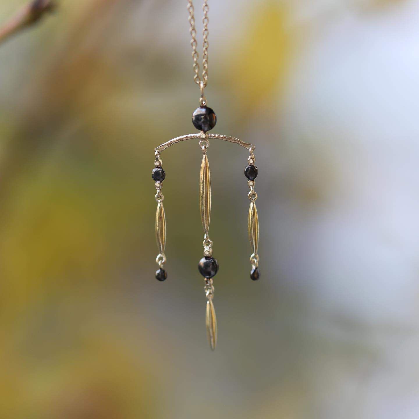 Collier pendentif en or avec perles noires et gouttes d'or allongées, suspendu à l'extérieur.