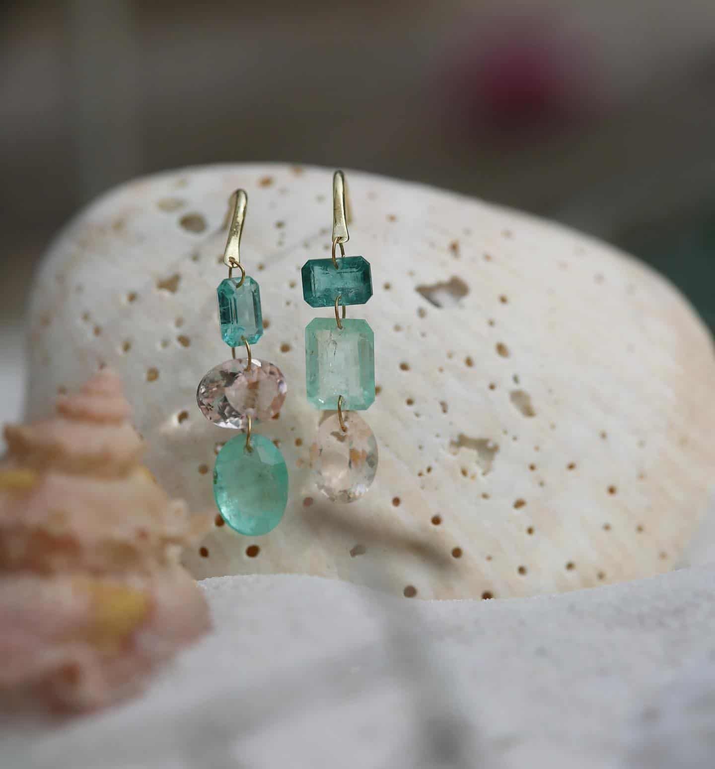 Boucles d'oreilles en or avec pierres précieuses aux tons bleu sarcelle et pêche sur un coquillage blanc texturé.