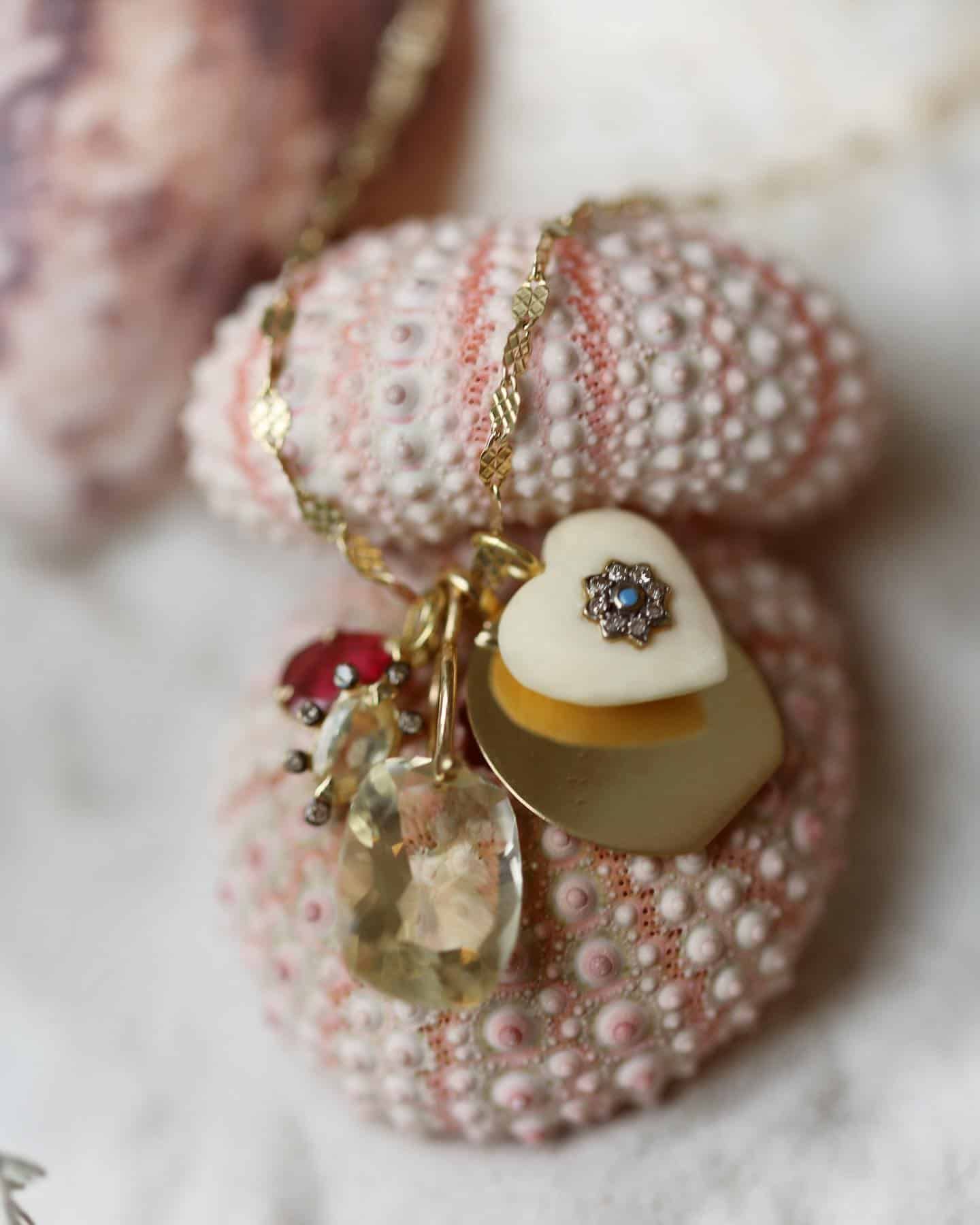 Collier en or avec breloques en forme de cœur et de pierres précieuses reposant sur des oursins roses.