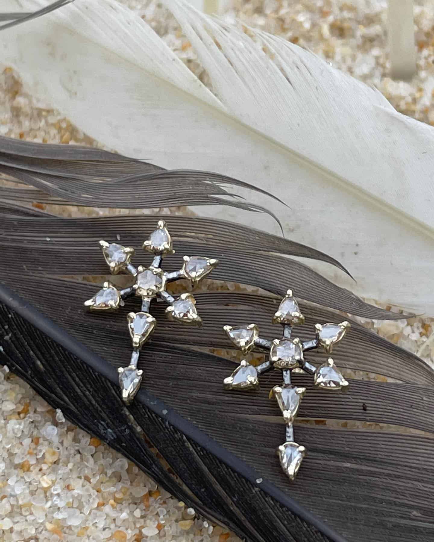 Boucles d'oreilles flocon de neige en argent sur une plume noire et blanche, posées sur une surface sablonneuse.