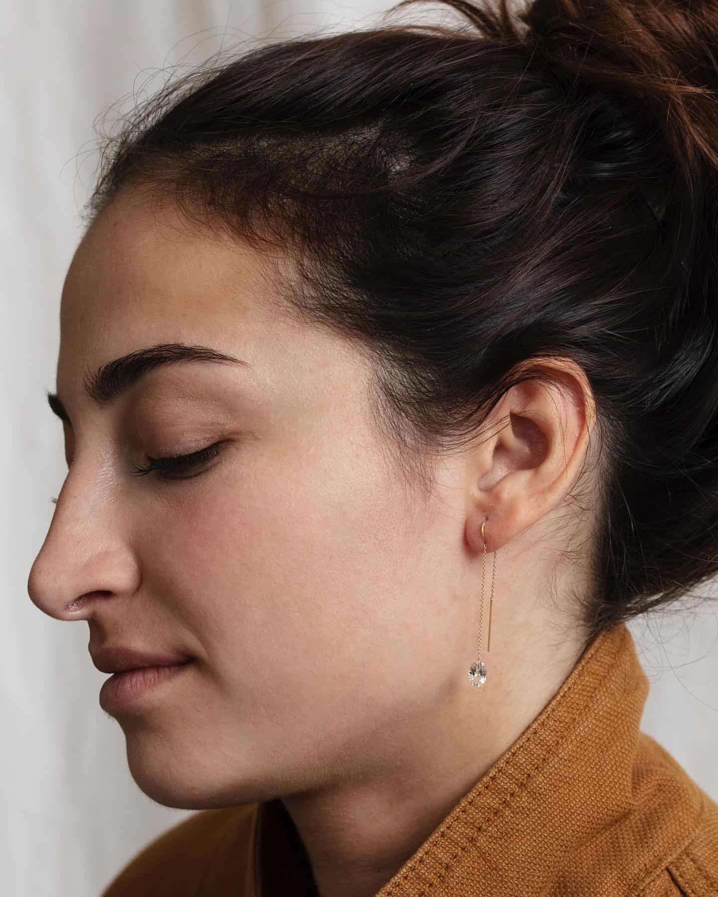 Femme aux cheveux noirs en chignon portant une boucle d'oreille en or, profil rapproché avec les yeux fermés.