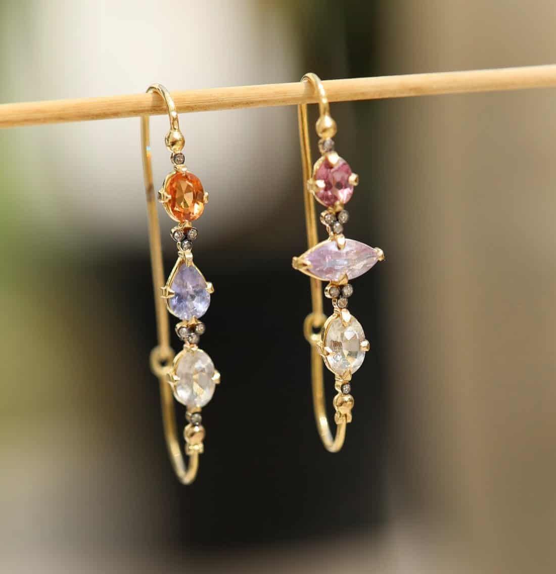 Boucles d'oreilles en or avec plusieurs pierres précieuses colorées suspendues à un fin bâton en bois.