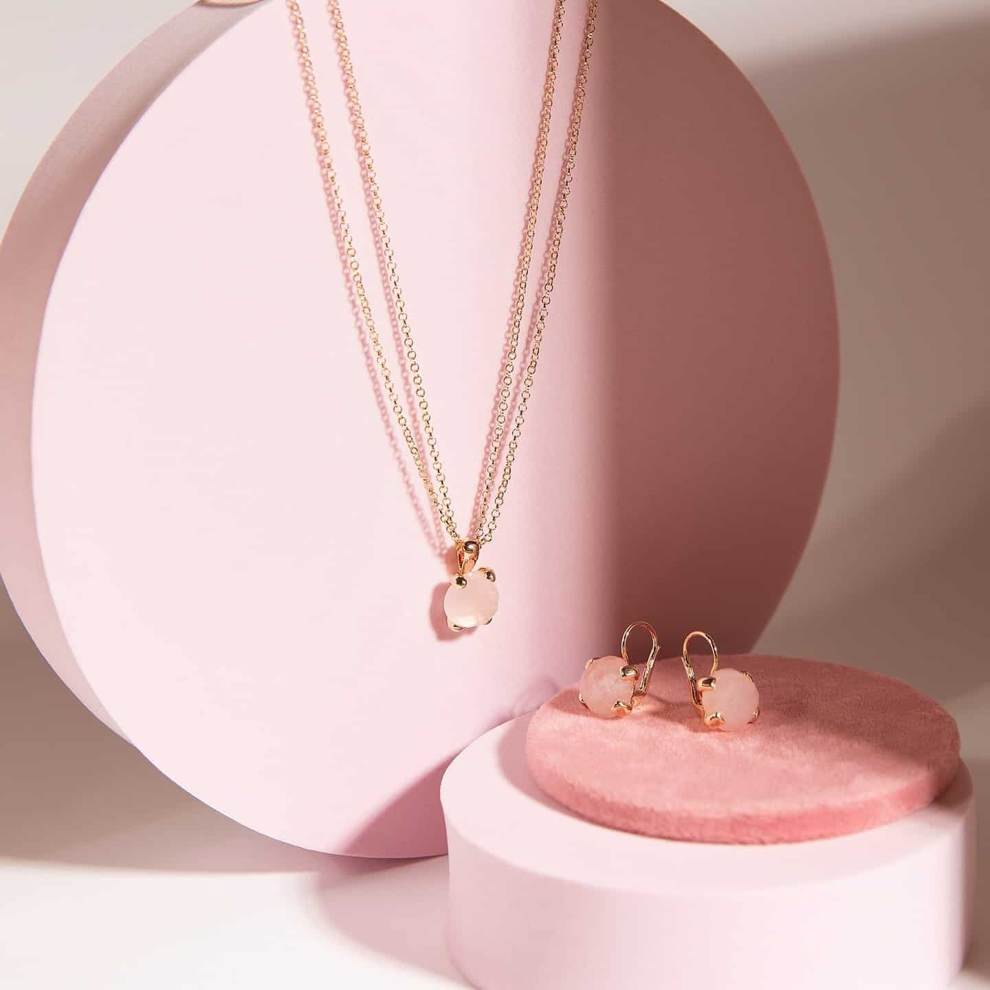 Collier et boucles d'oreilles en or rose avec pierres roses sur présentoir rose.