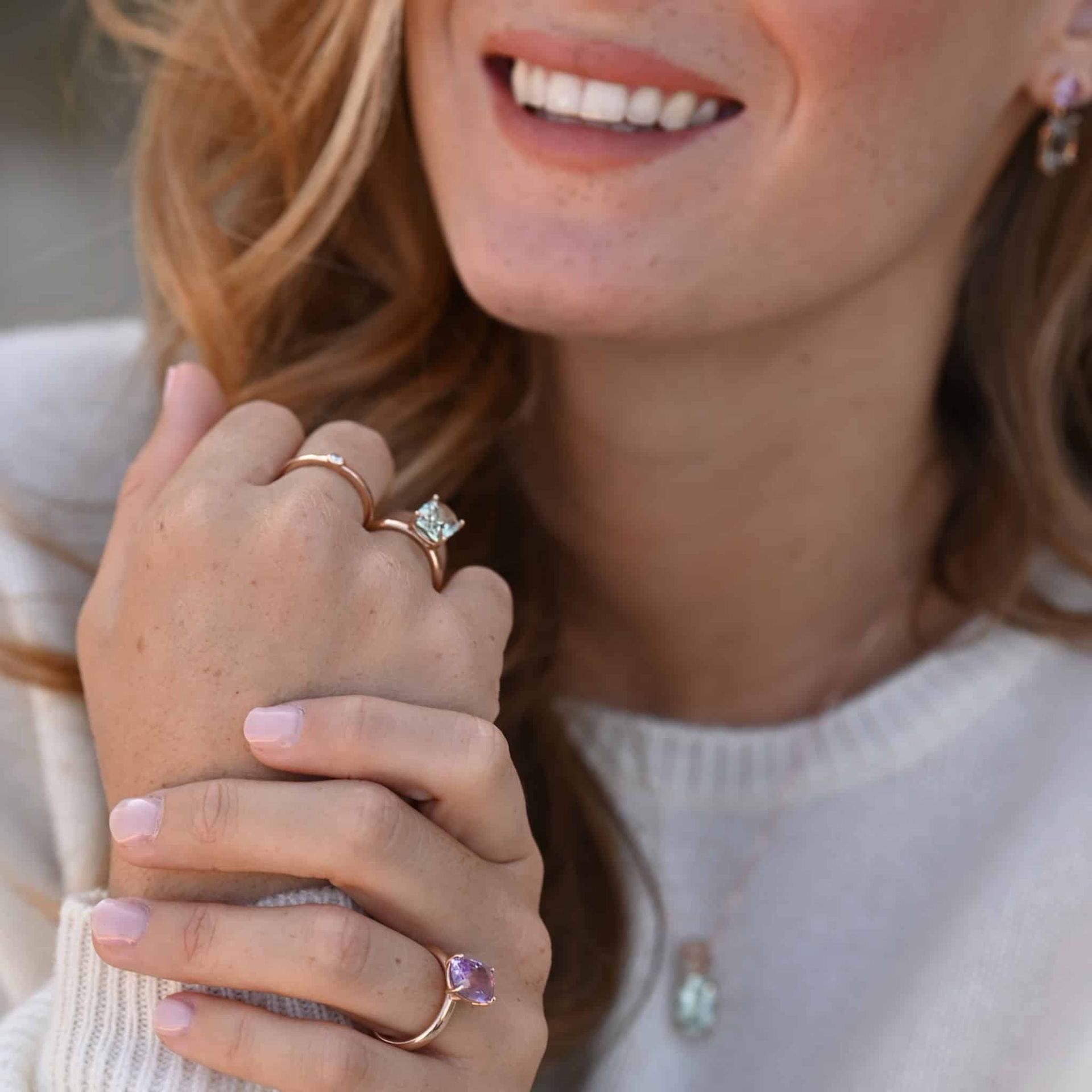 Femme montrant des bijoux, souriante, à l'intérieur, portant un pull.