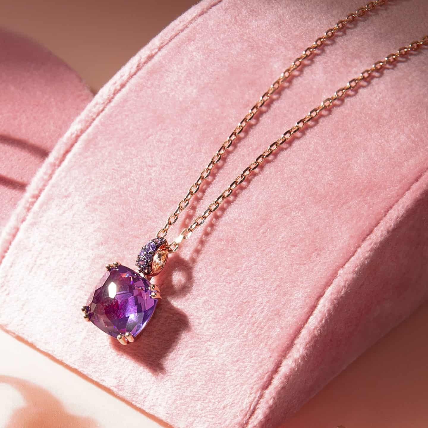 Collier en or avec un grand pendentif en pierre précieuse violette sur une surface en velours rose.