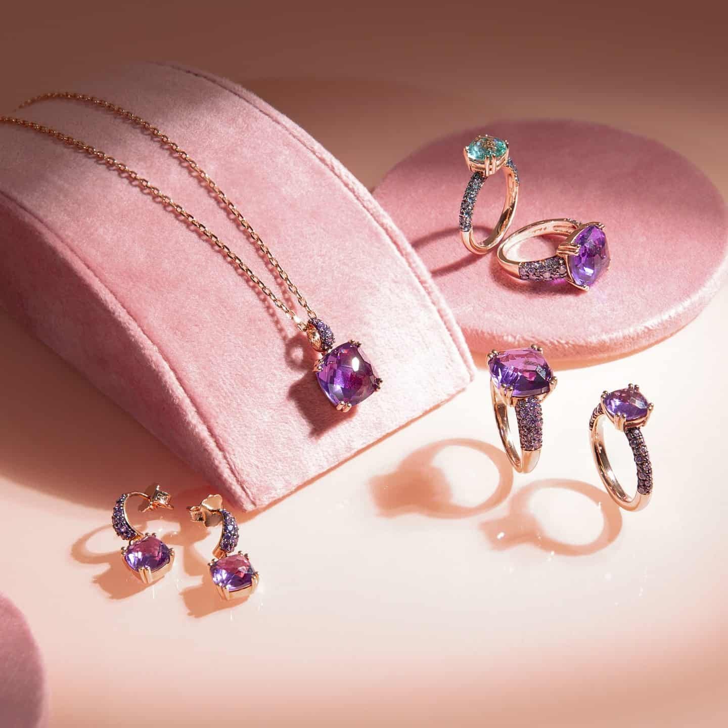 Présentoir à bijoux avec collier, boucles d'oreilles et bagues ornés de pierres précieuses violettes sur un support rose.
