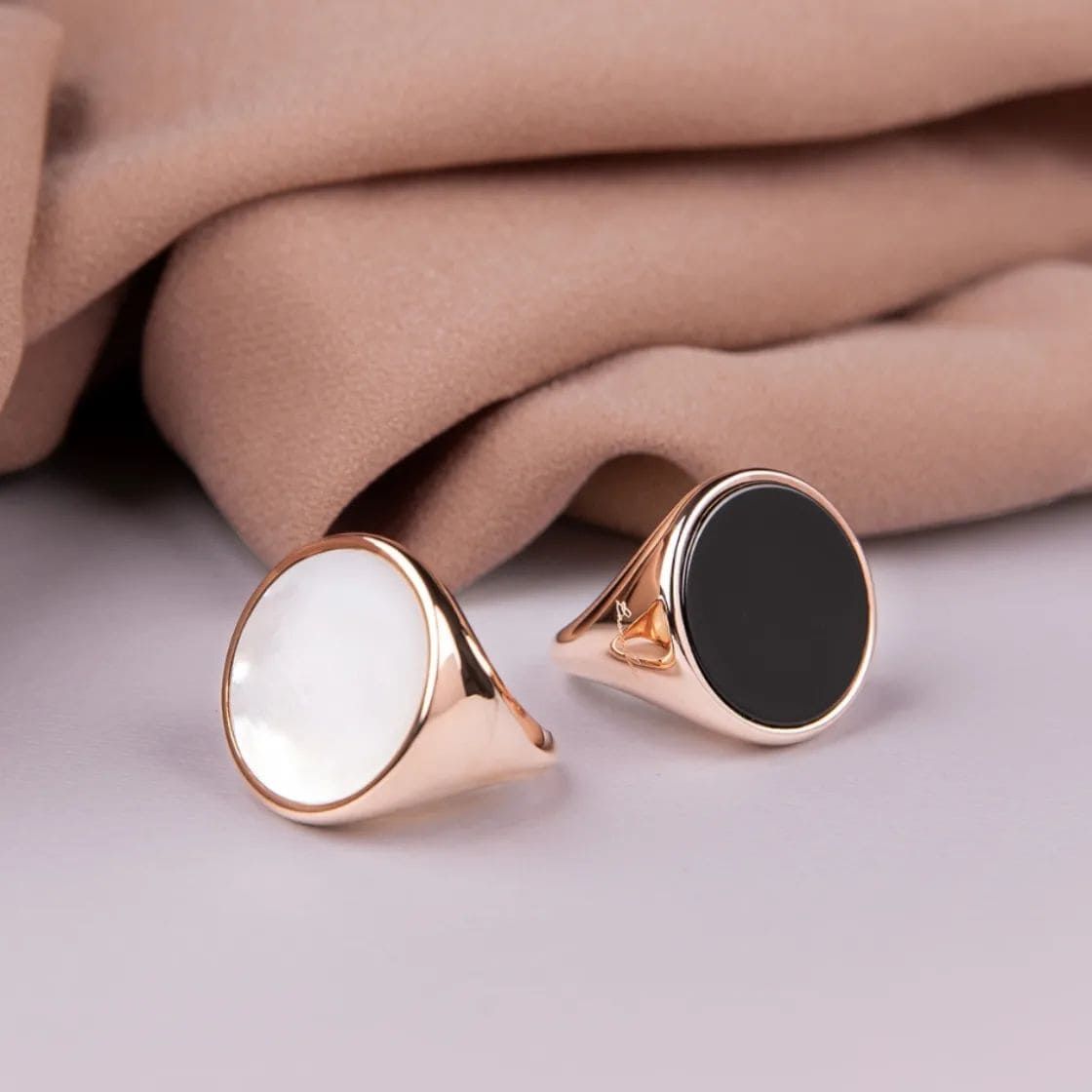 Deux chevalières, une blanche, une noire, sur une surface réfléchissante, avec un fond en tissu beige.