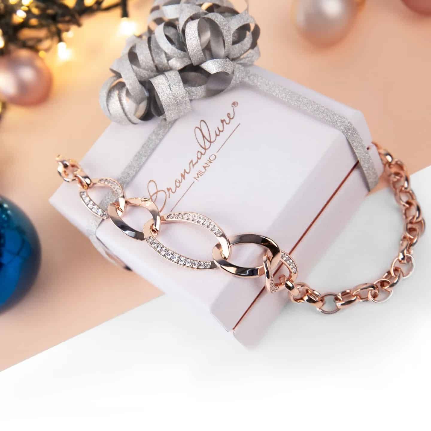 Bracelet chaîne en or rose sur une boîte cadeau emballée avec un nœud, des décorations de Noël en arrière-plan.