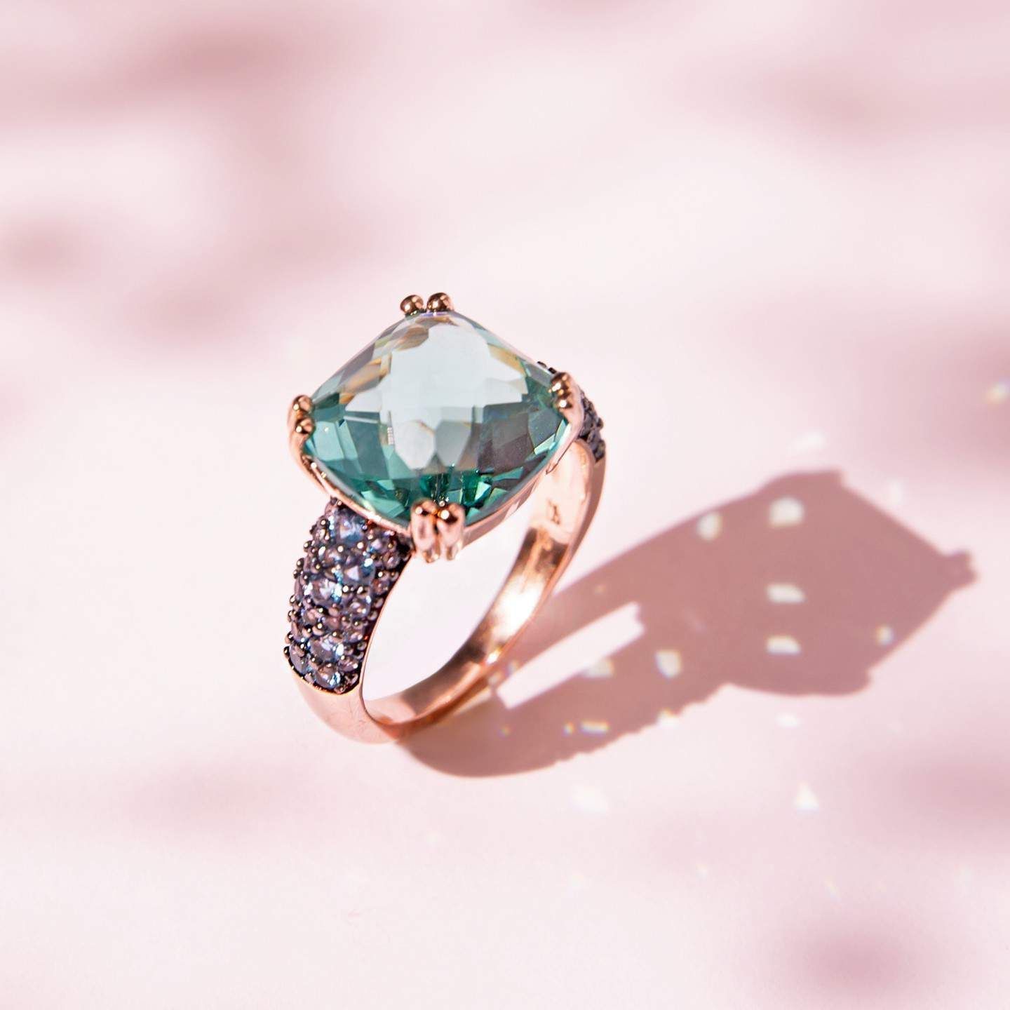 Bague en or rose avec une grosse pierre précieuse vert clair et des pierres plus petites et plus foncées sur la bande.