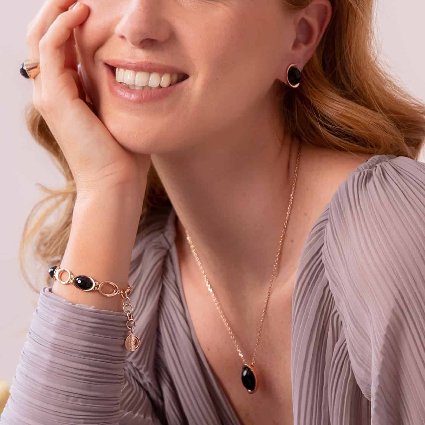 Femme portant des bijoux en or avec des pierres noires, souriante.