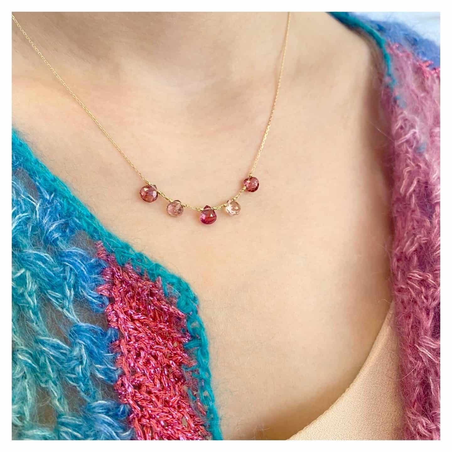 Femme portant un collier en or avec des pierres précieuses roses et un châle coloré bleu et rose.