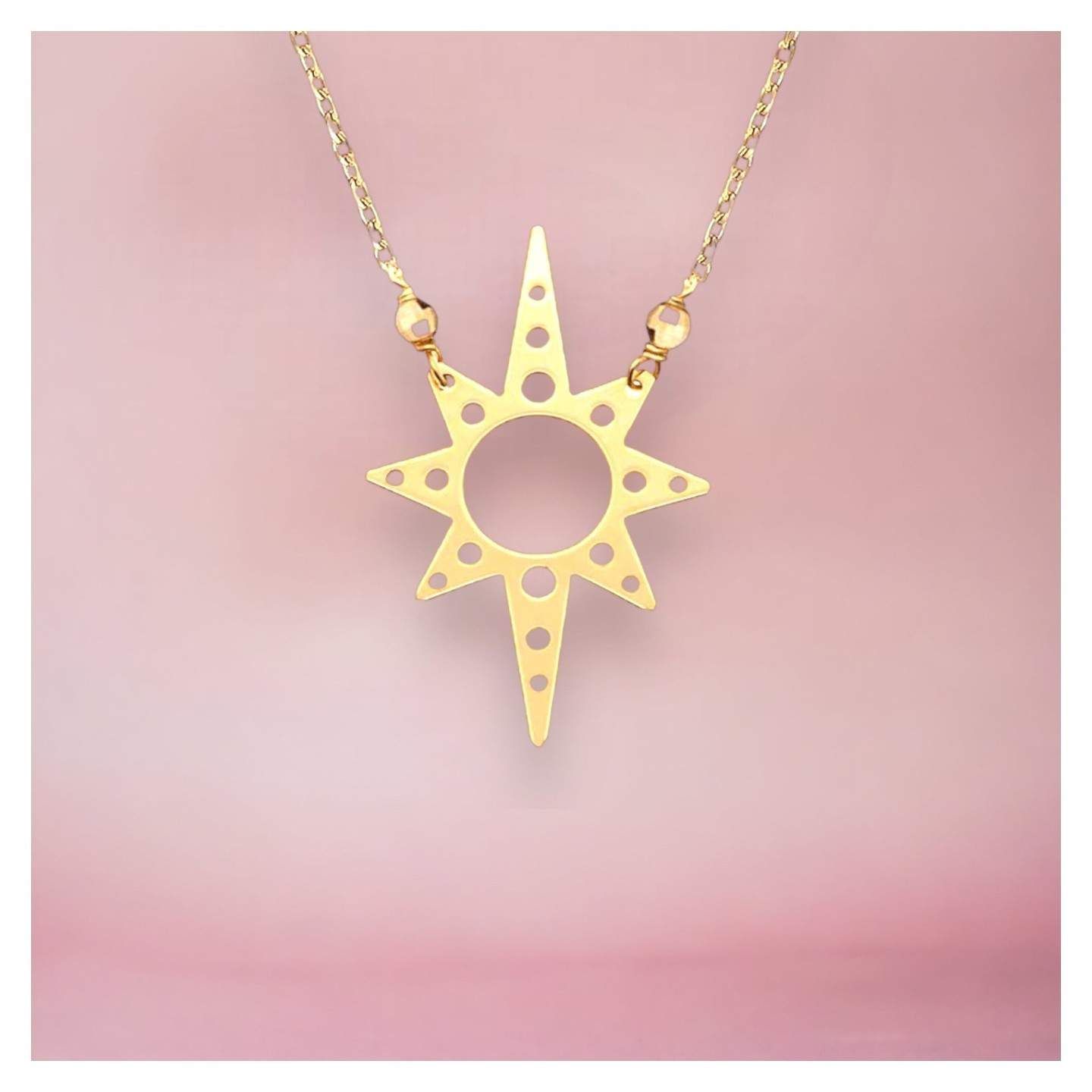 Collier pendentif étoile dorée sur fond rose.