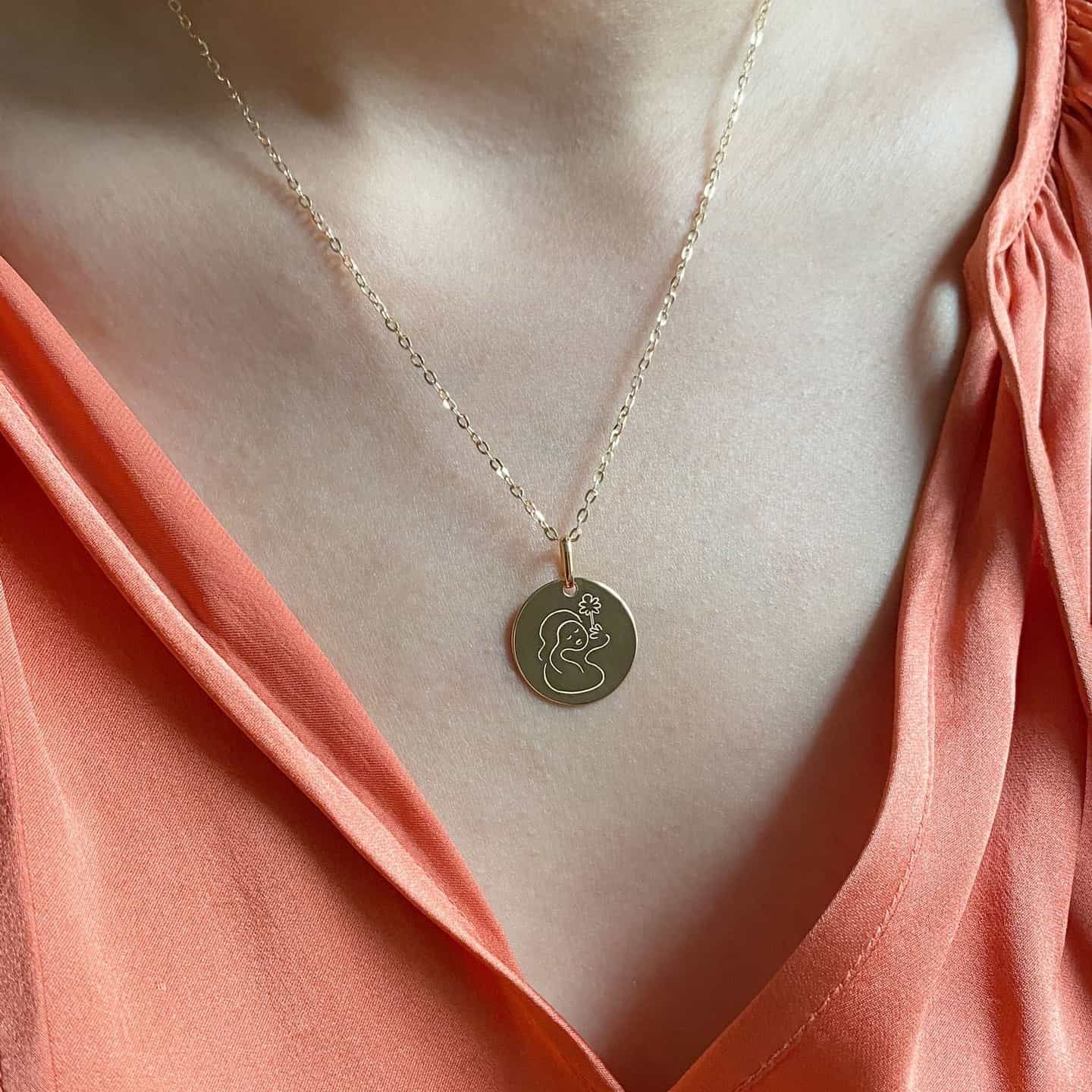 Femme portant un collier pendentif en forme de pièce d'or avec un haut rose.