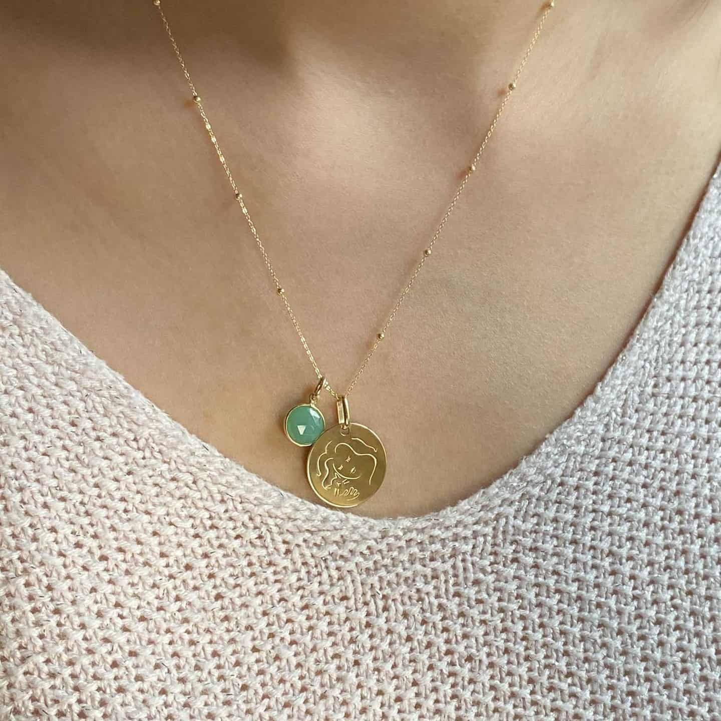 Femme portant un collier en or avec un pendentif rond et une pierre verte, gros plan.