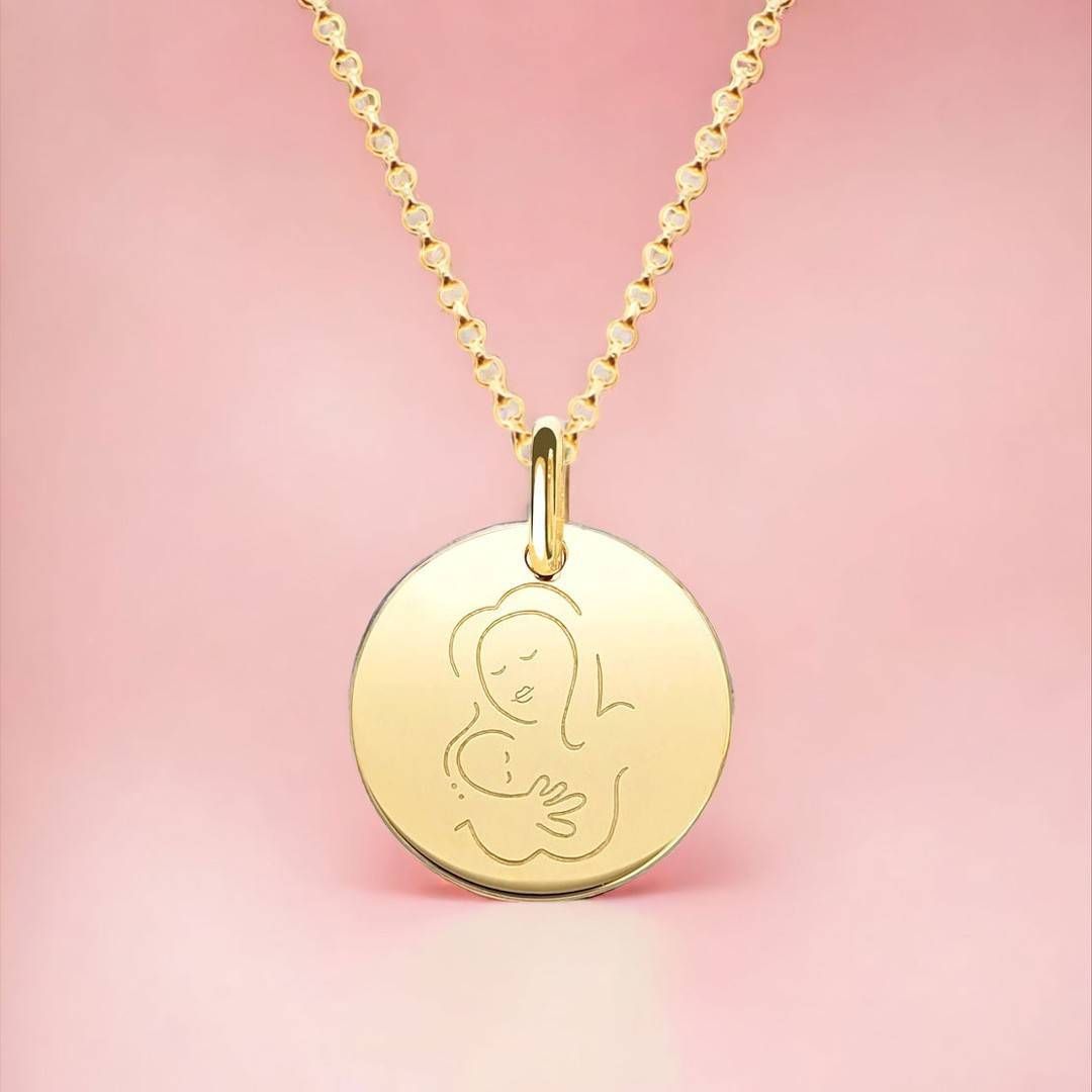 Collier en or avec pendentif rond représentant une mère et son enfant enlacés sur fond rose.