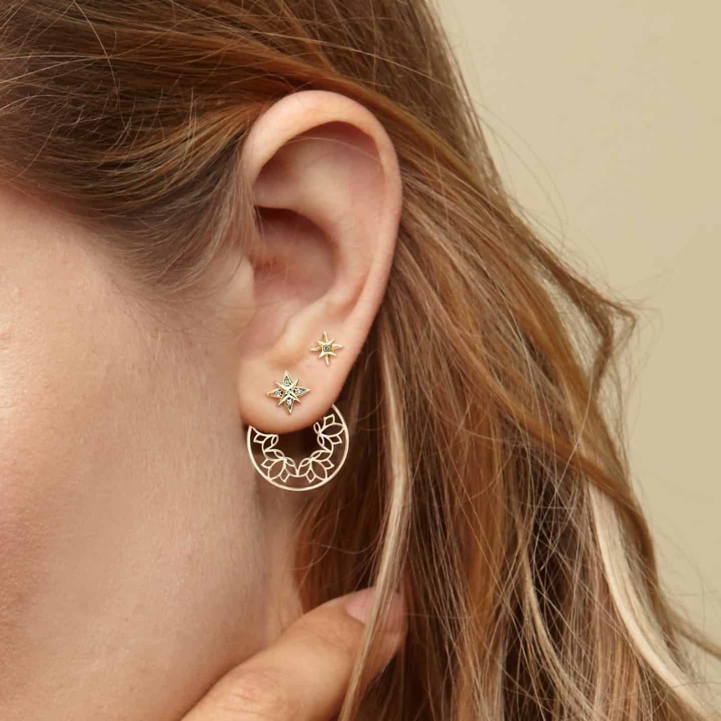 Oreille de femme avec trois boucles d'oreilles en or ; un créole floral et deux clous d'oreilles en étoile.