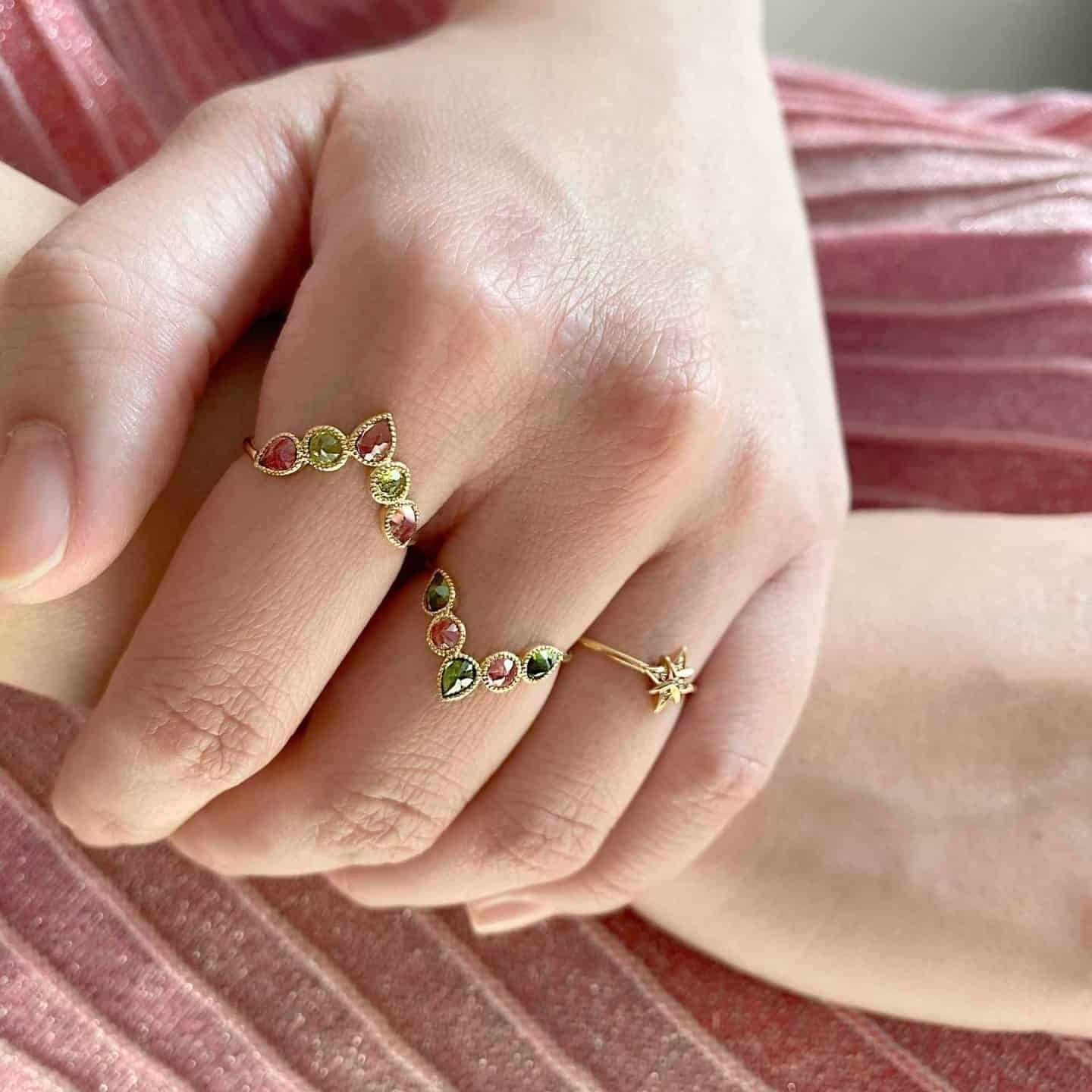 Main portant deux bagues : une bague en pierre précieuse colorée et une bague en forme d'étoile, gros plan.