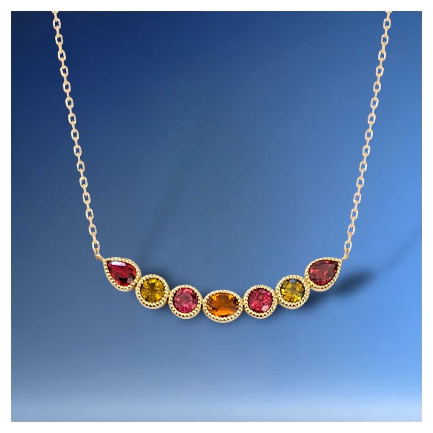 Collier en or avec une rangée de pierres précieuses colorées sur fond bleu.