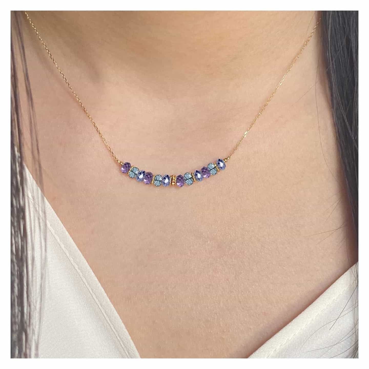 Femme portant un collier en or avec une rangée incurvée de pierres précieuses violettes et bleues.