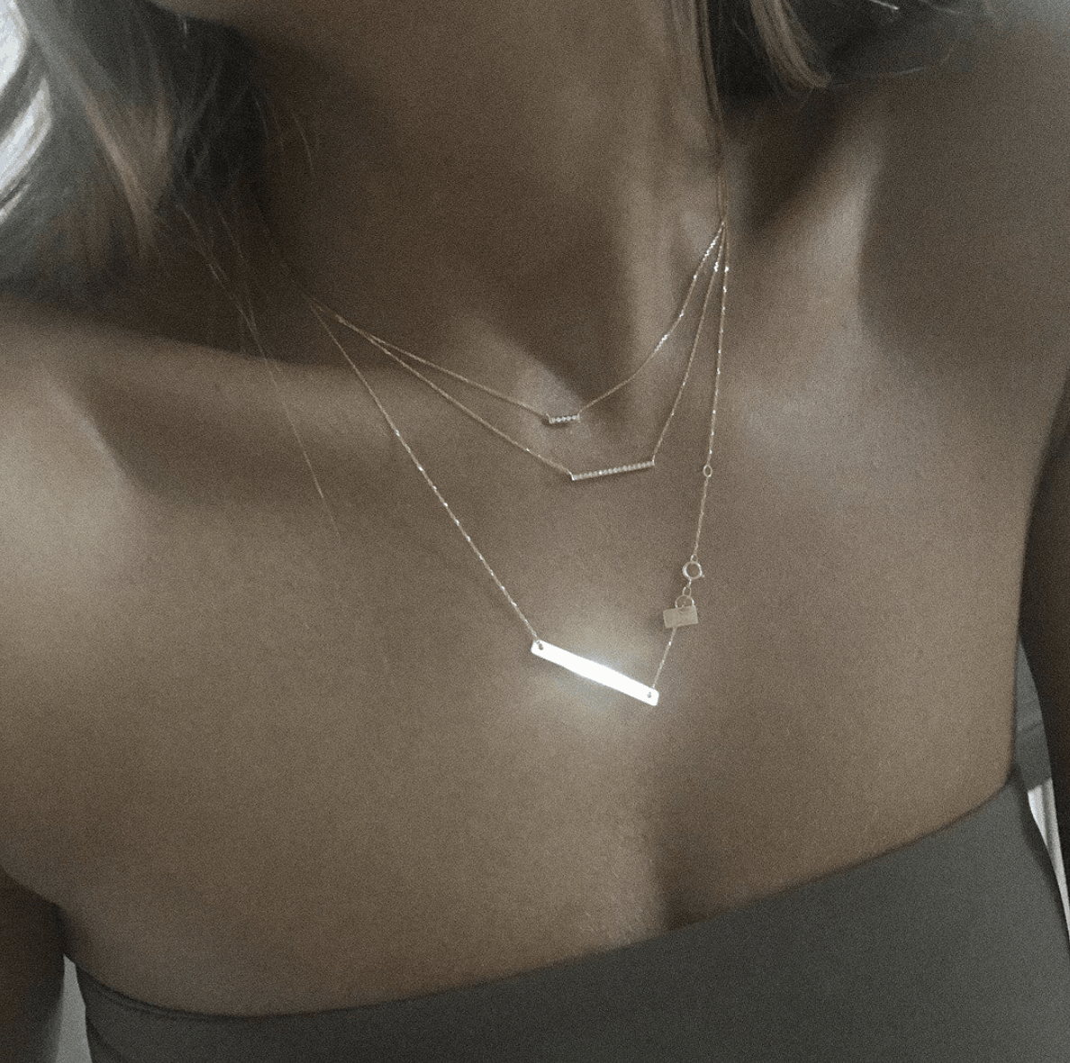 Femme portant trois colliers en or superposés sur sa poitrine.