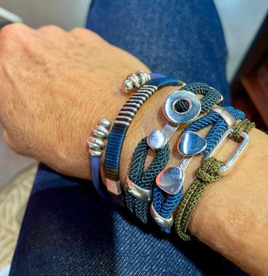 Femme en pull blanc, plusieurs bagues et bracelets, posée les mains jointes, à l'intérieur.