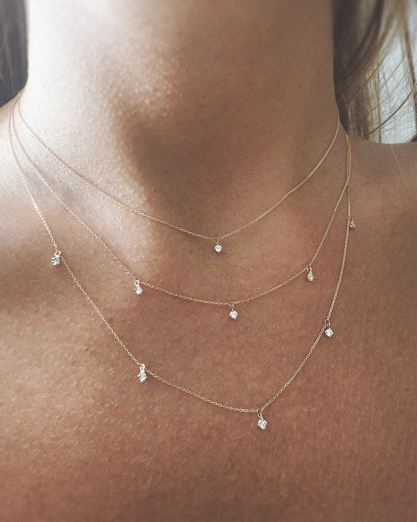Femme portant des colliers en or superposés avec des pendentifs circulaires et en forme de barre, chemise blanche.