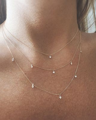 Femme portant des colliers en or superposés avec des pendentifs circulaires et en forme de barre, chemise blanche.