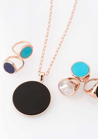 Parure de bijoux en or rose : collier avec pendentif noir, bagues avec turquoise, perle et pierres noires.