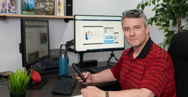 A man is sitting at a desk in front of two computer monitors with web design program open