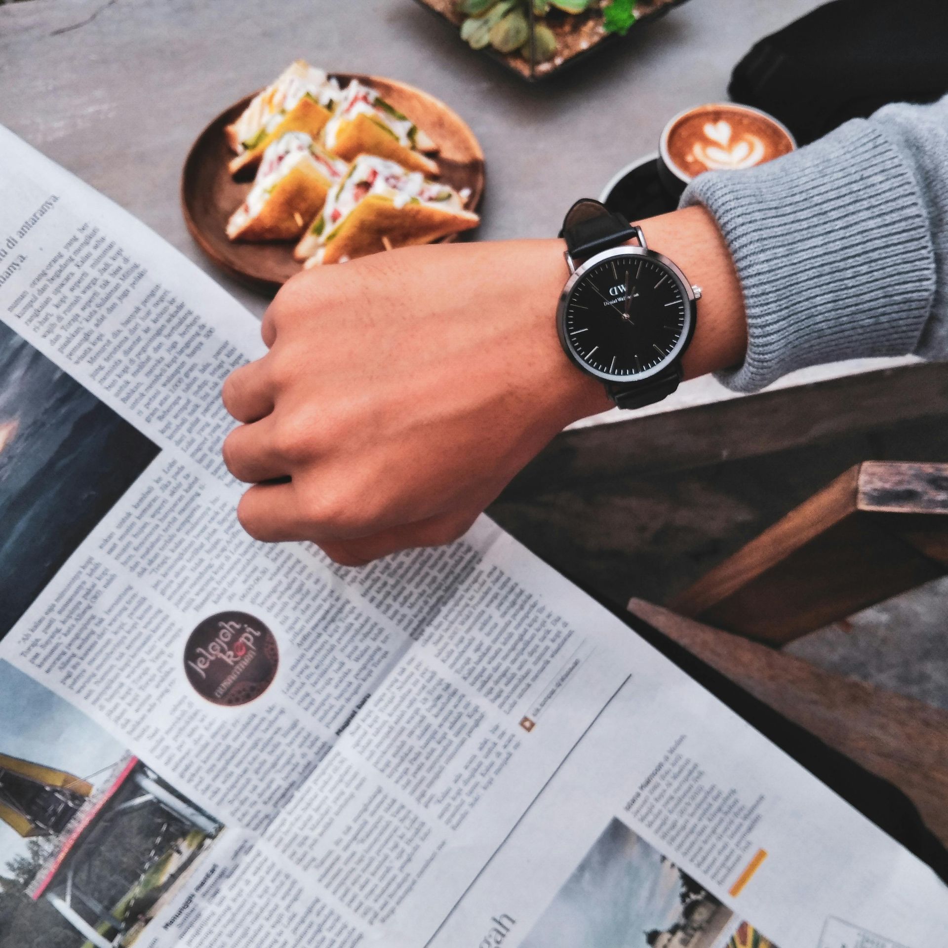 A person wearing a watch is reading a newspaper