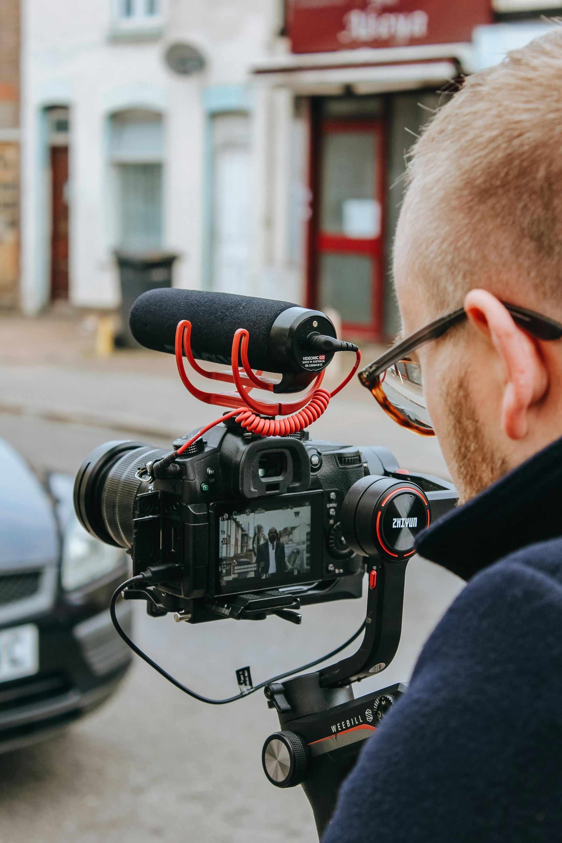 A man is taking a video of a car with a camera.