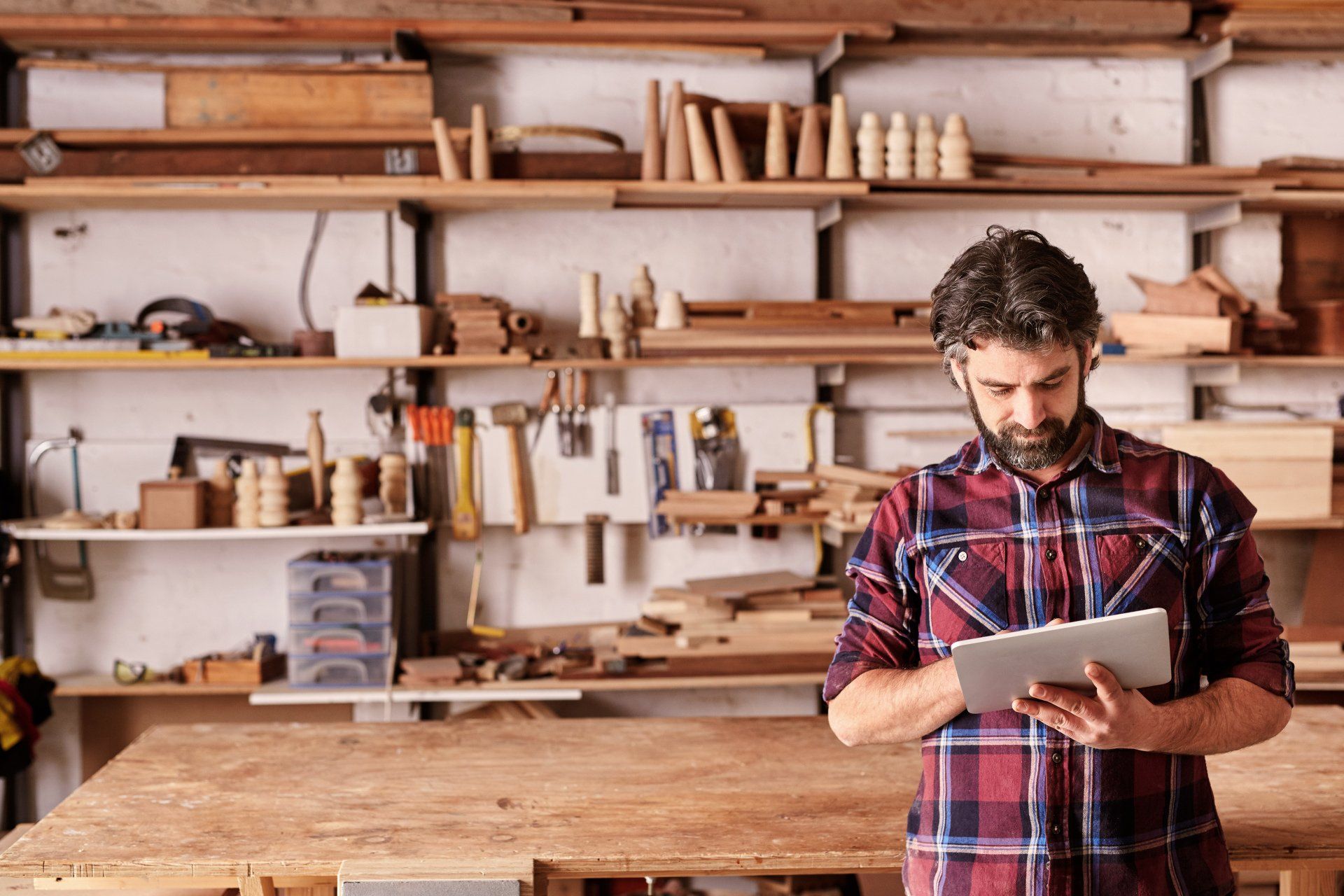 A man is using a tablet in a woodworking shop.