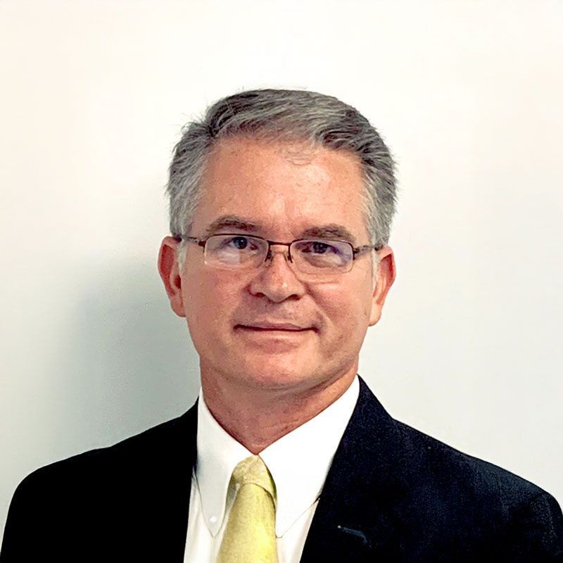 Pastor Bobby Creel with glasses and tie in a suit, smiling in front of a church interior.