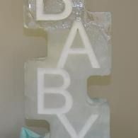 Clear plastic toy blocks spelling “BABY” in white letters on a beige surface.