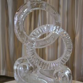 Transparent interlocking glass rings on a reflective surface with beige curtains behind them