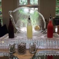 Clear beverage dispenser with yellow and red drinks on a mirrored table at an event display