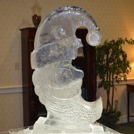Translucent ice sculpture shaped like a crescent moon but with a Santa face and hat on a table.