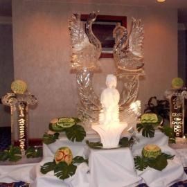 Twin ice sculptures with Swans with a white statue in front, flowers, and greenery