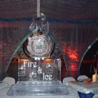 Ice sculpture reading “Fire & Ice” on a stage, lit by colorful event lights and surrounded by candles.