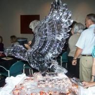 Large reflective ice sculpture on a table, with people standing around it in an indoor room