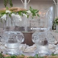 Transparent acrylic sign and clear glass jars on a decorated white table with greenery and flowers.