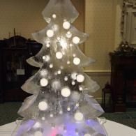 Translucent ice sculptured Christmas tree with glowing white lights and ornaments in a dim room