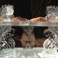 Ice sculptured dessert display with silver bowls, glass stands, and copper-colored treats on a mirrored table