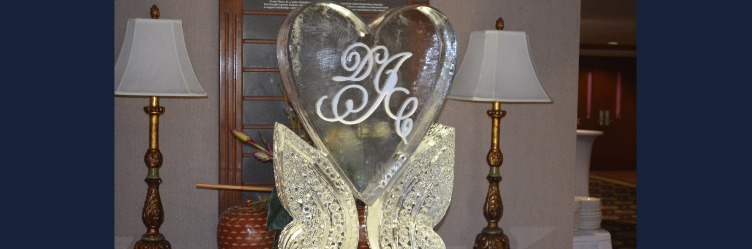 Decorative ice sculptured heart with monogram and butterfly wings on a table between two lamps