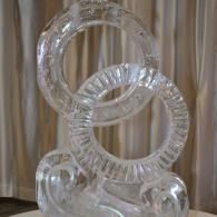 Clear glass-like ice sculptural rings stacked on a reflective base against curtains