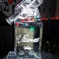 Clear decorative bottle-shaped ice sculpture with a tilted top in a dimly lit room.