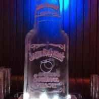 A lit glass bottle on a bar with blue and red neon reflections and a white logo label.