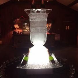 Glowing white fountain ice sculpted centerpiece in a dimly lit room with warm amber lights and dark walls