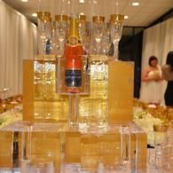 Tower of stacked liquor bottles and champagne flutes on a banquet table, with two blurred people in the background