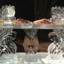 Mirrored sea horse ice sculptured pedestal trays holding shrimp, lit against a dark background